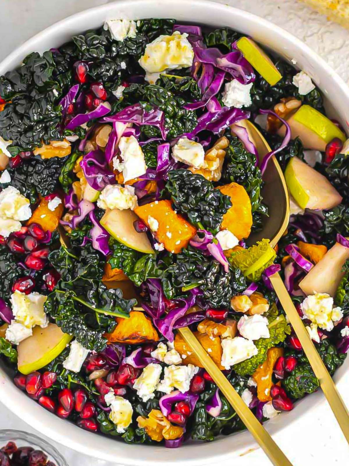 Healthy butternut squash kale salad with honey mustard dressing walnuts apple and pomegranate close up.
