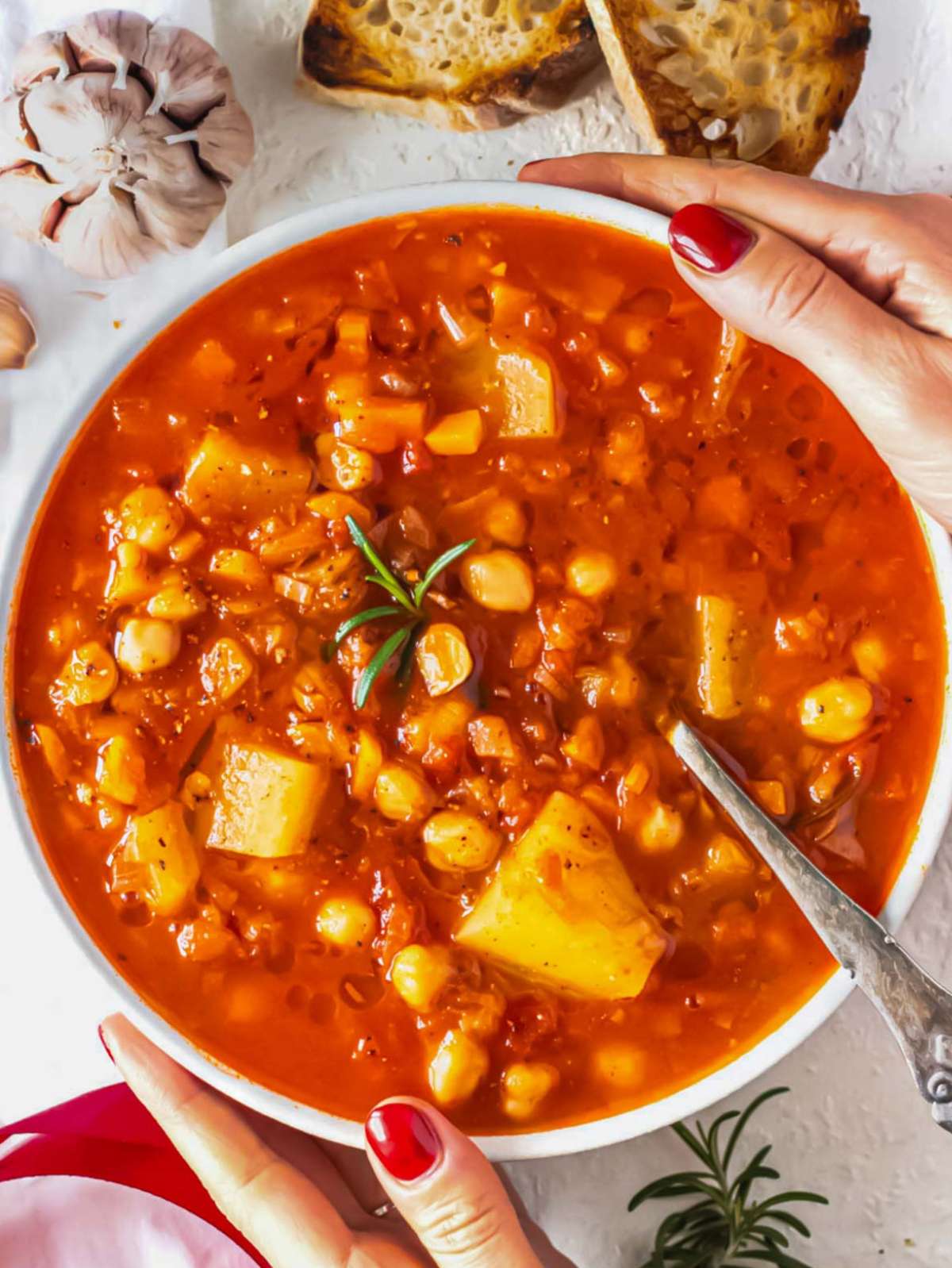 Louise holding a bowl of rustic mediterranean chickpea soup served with crusty bread.