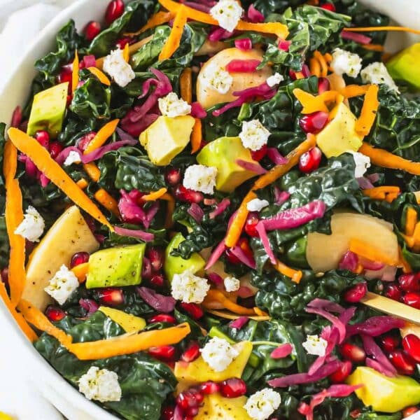 Mediterranean kale salad with feta cheese apple avocado and pomegranate on white table.
