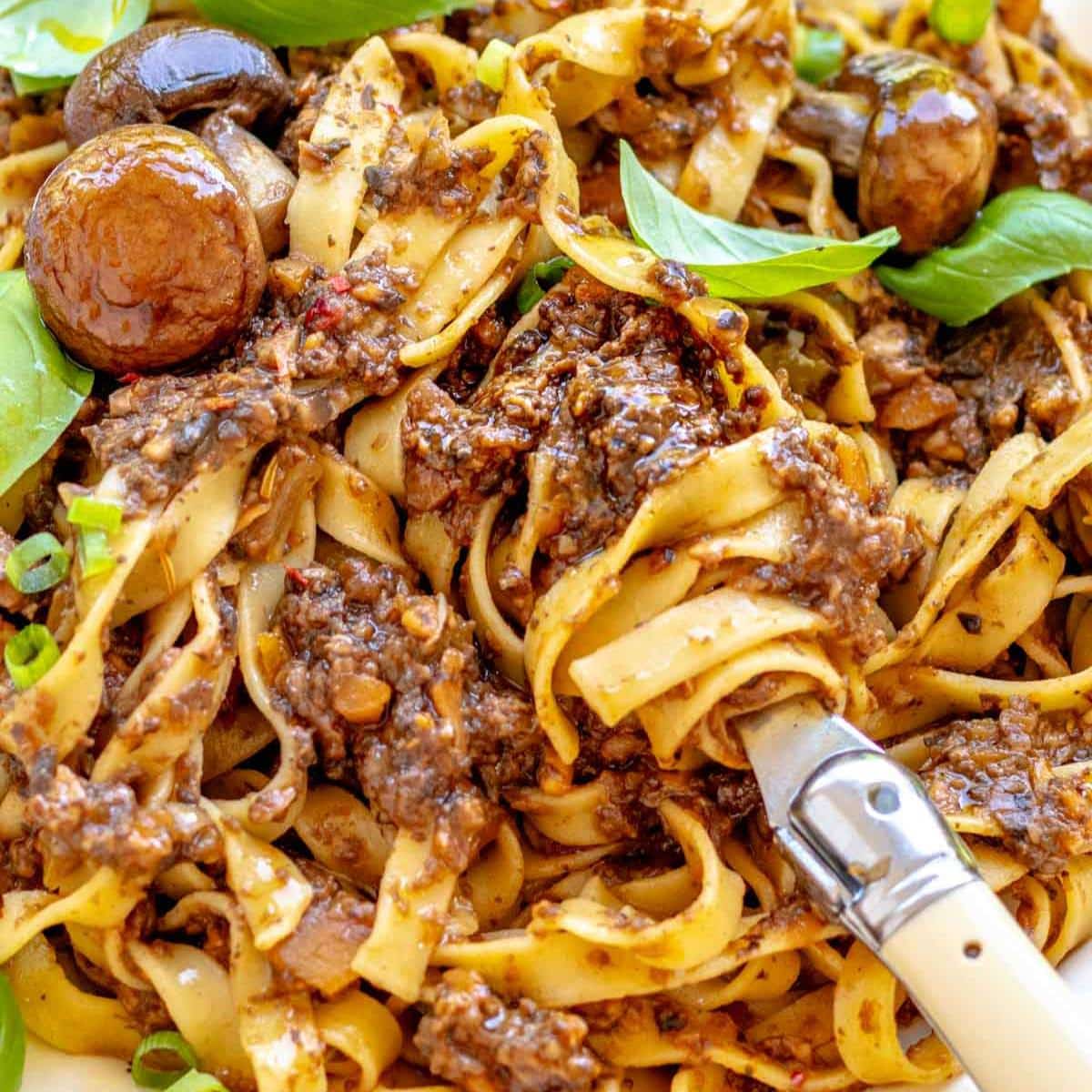 Mediterranean mushroom pasta with tomato based ragu served in a white bowl with fresh basil.