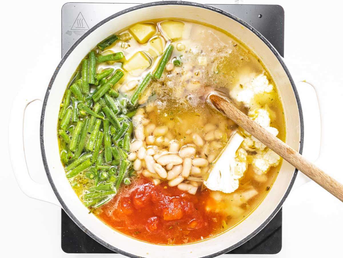 Step 2 Adding broth beans potatoes cauliflower and green beans to pot for homemade vegetable soup.
