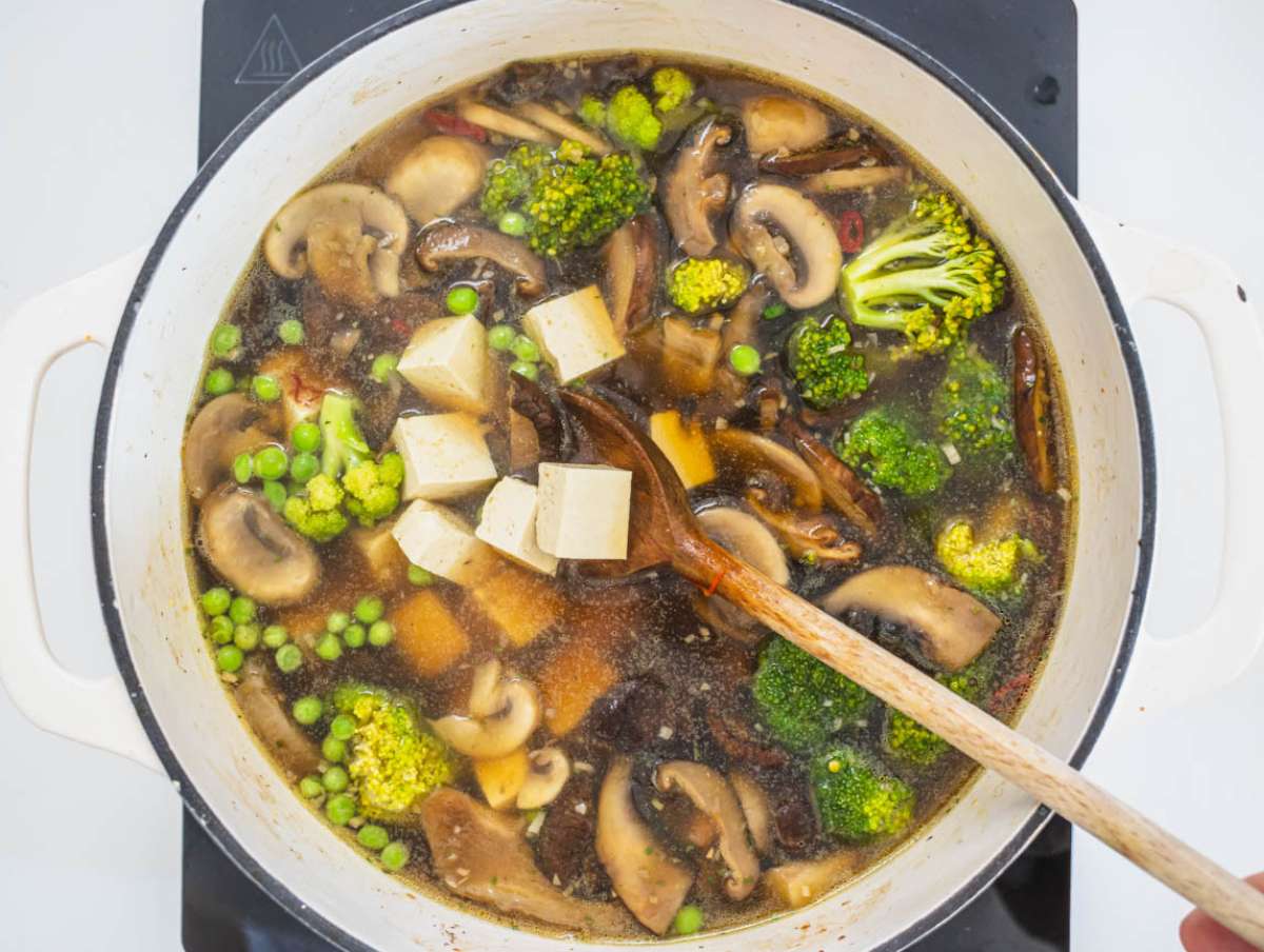 Step 3 Adding broth tofu broccoli and peas to pot for hearty tofu mushroom soup recipe.