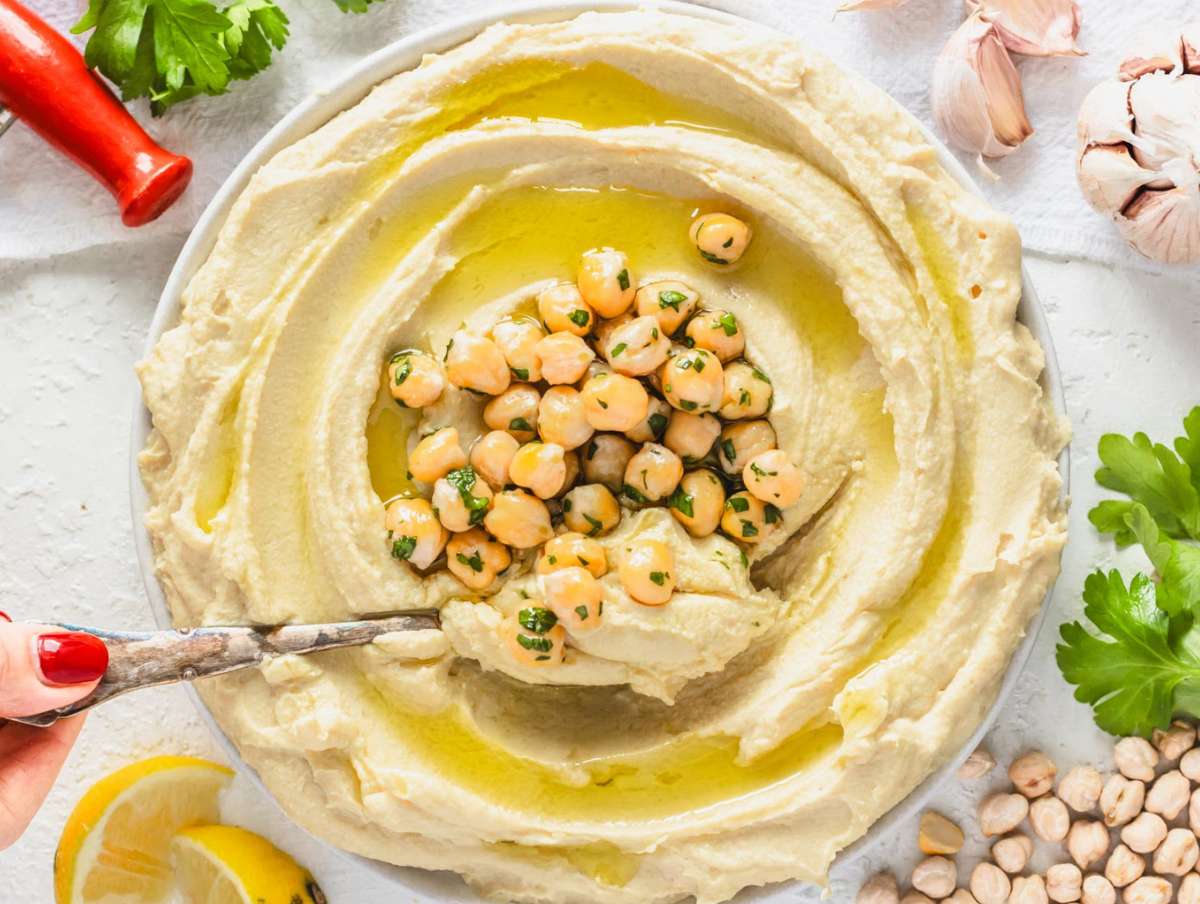 Step 3 Homemade hummus served in bowl swirled topped with chickpeas parsley and olive oil drizzle.