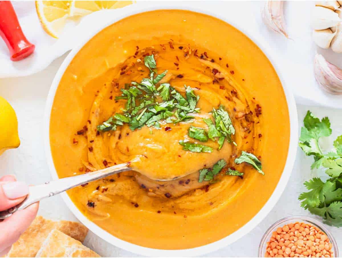 Step 4 serving lentil soup in a bowl garnished with lemon juice, chili oil, and parsley.