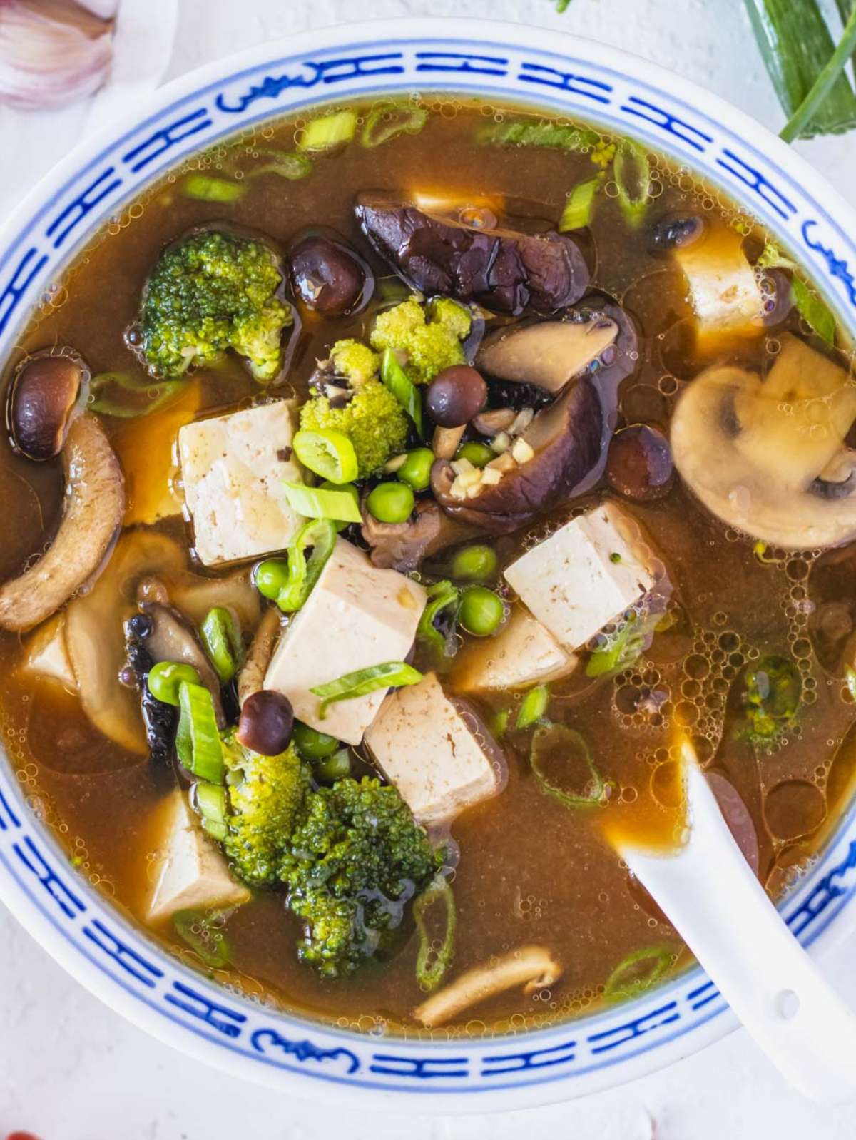 Top down tofu mushroom soup bowl with mushrooms tofu broccoli and peas in light broth.