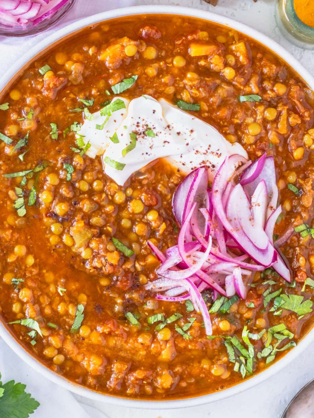 Top down view of hearty spiced lentil soup served with yogurt and fresh herbs.