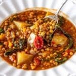 Warm bowl of Mediterranean lentil soup with bread on rustic wooden table.