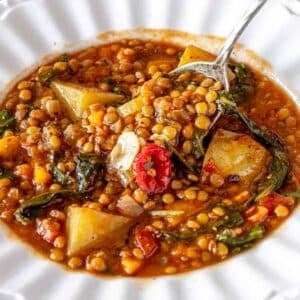 Warm bowl of Mediterranean lentil soup with bread on rustic wooden table.
