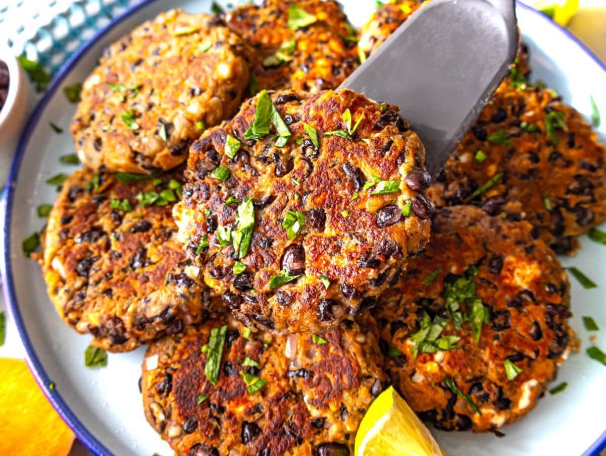 Black bean patties with feta and herbs served on a plate with lemon.