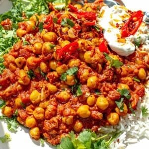 Chickpea masala on a plate with rice fresh herbs and lemon wedges on the side.