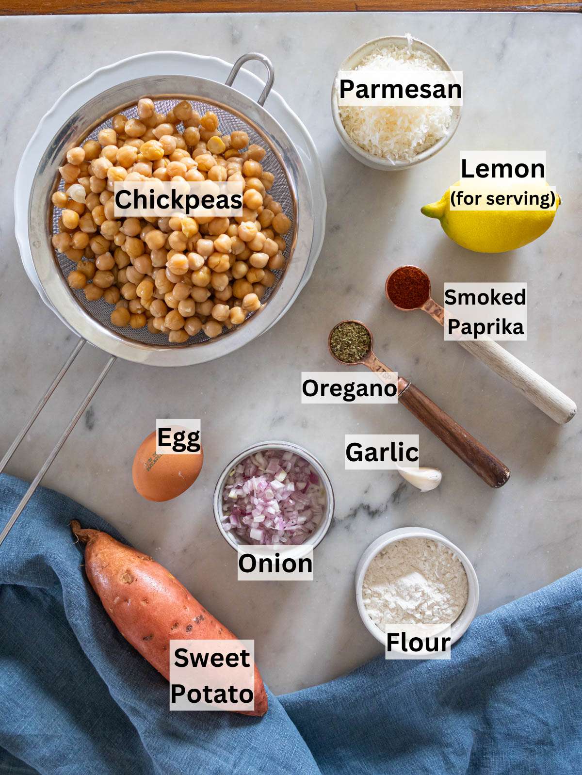 Chickpeas, sweet potato, flour, egg, parmesan, onion, and spices arranged on a kitchen counter.