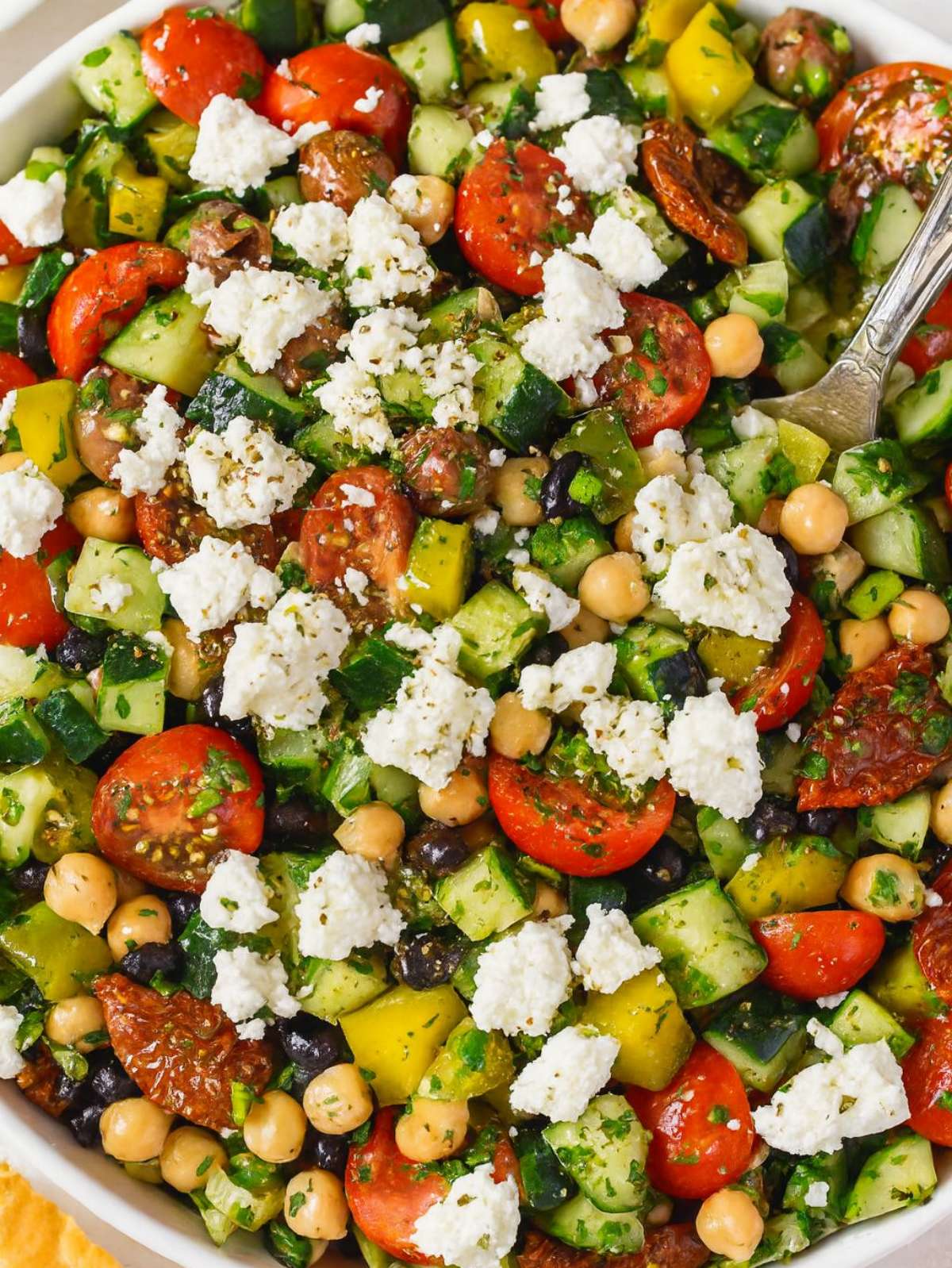 Close up of Mediterranean bean salad with chickpeas, feta, and colorful vegetables in a white bowl.