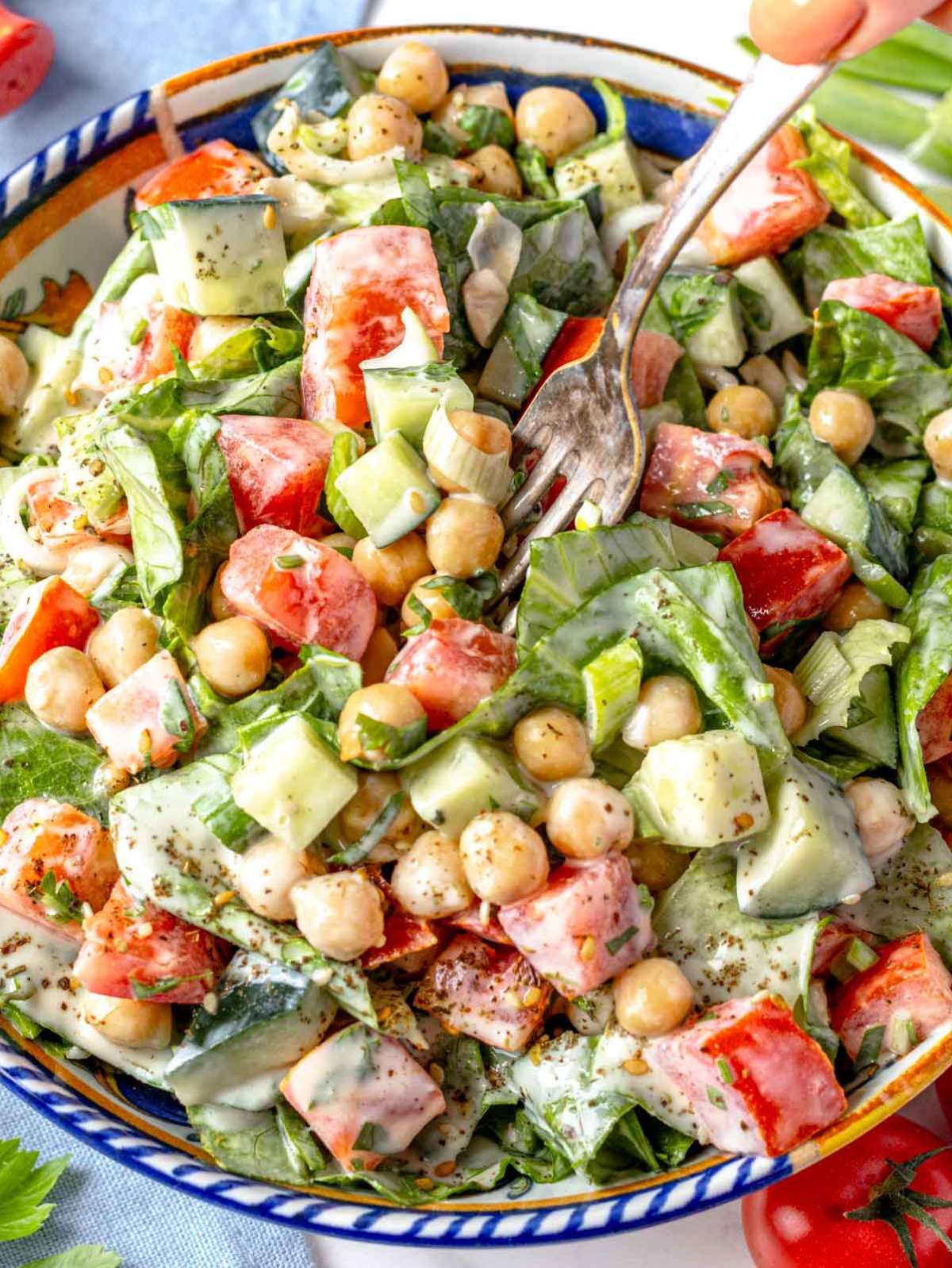 Close up of chopped chickpea salad with creamy tahini dressing and fresh vegetables.