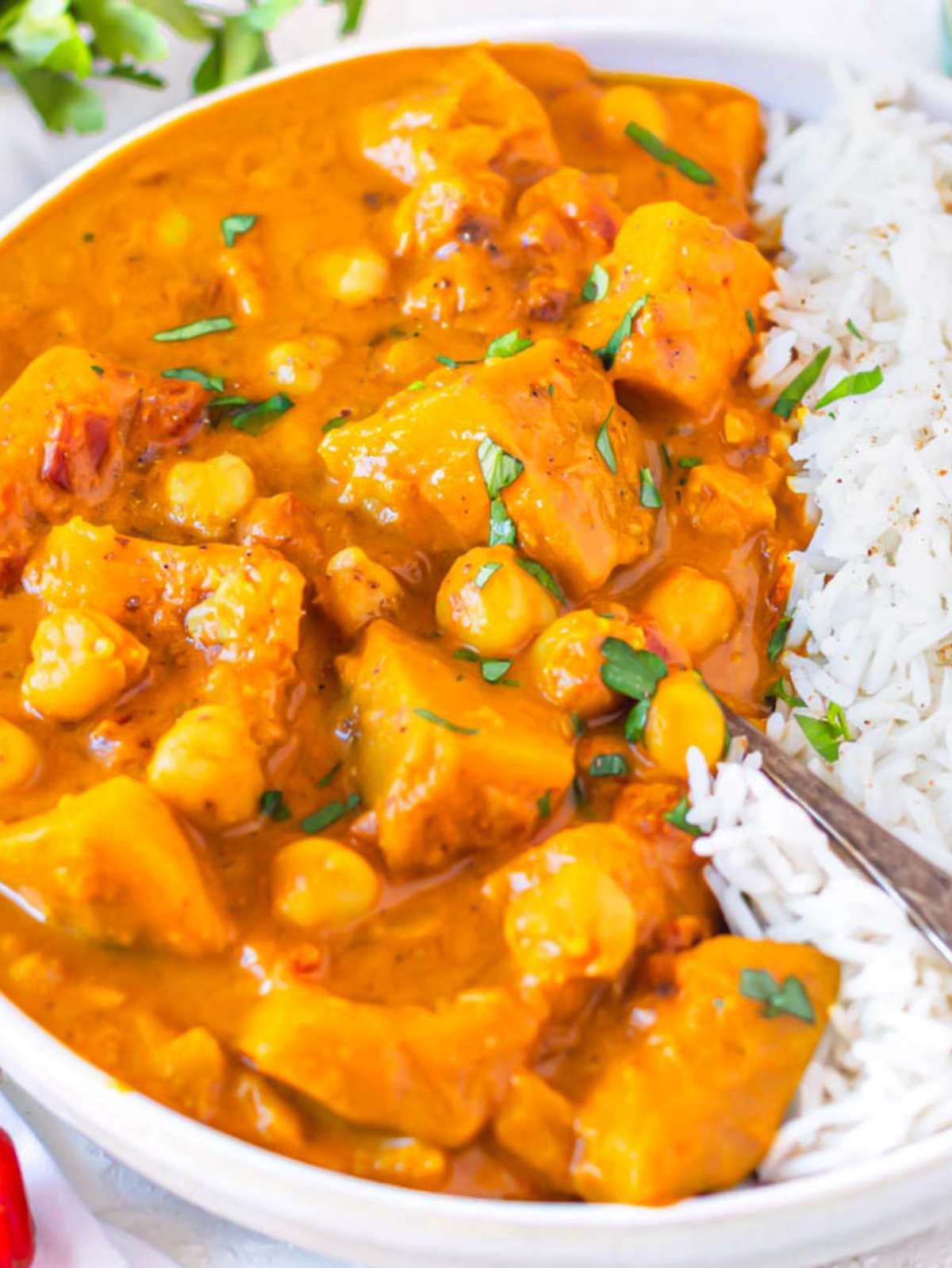 Close up of creamy butternut squash chickpea curry served in a white bowl with basmati rice.