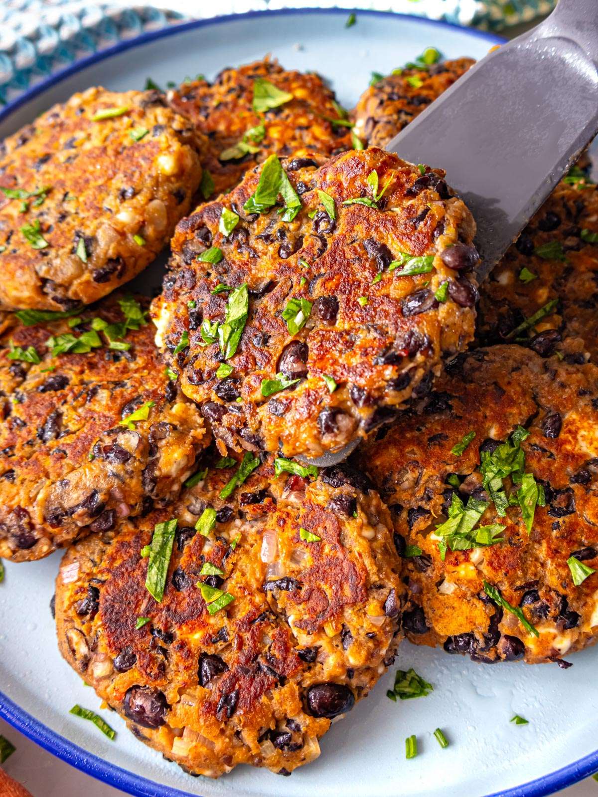 Close up of crispy black bean patties stacked on a plate with yogurt dip.