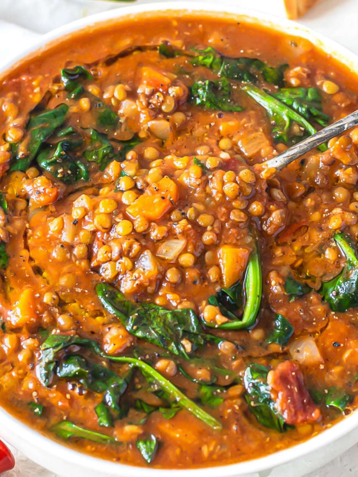 Close up of spinach lentil soup showing hearty lentils, spinach, and rich tomato broth.