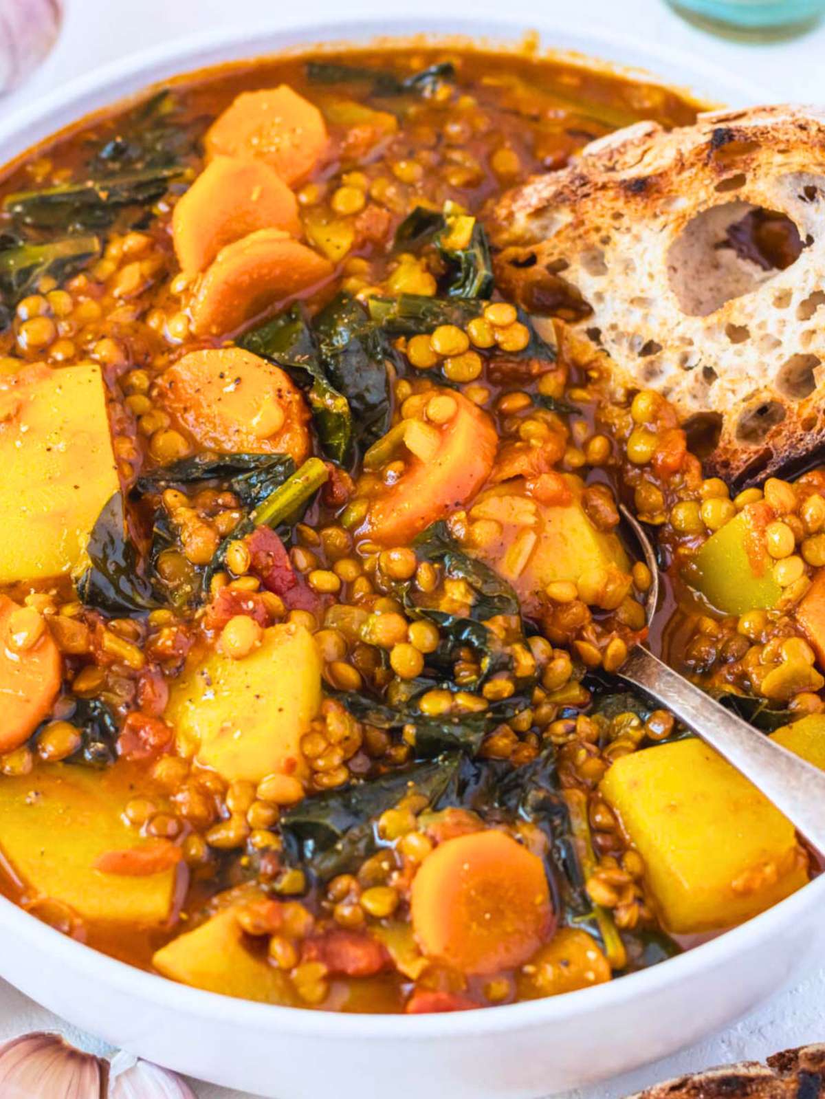 Close up of turmeric lentil soup with spinach and potatoes in a white bowl.