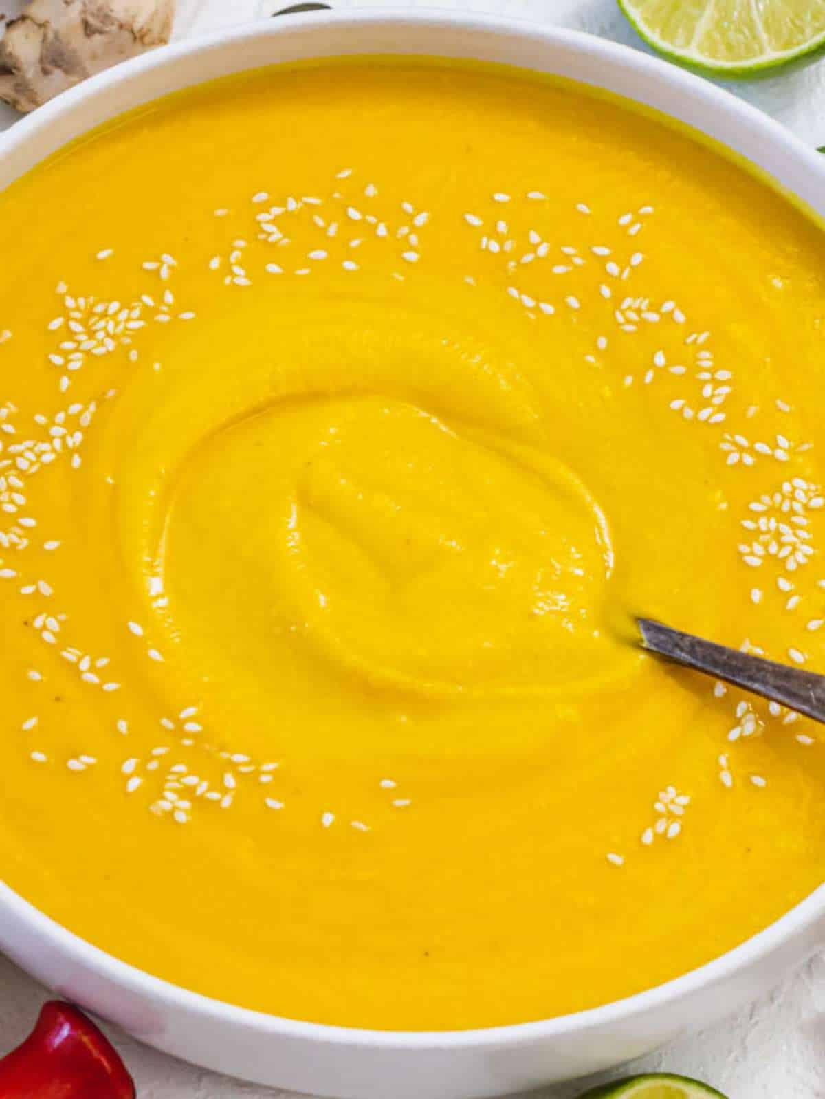 Creamy coconut pumpkin soup served in a bowl with lime on top.
