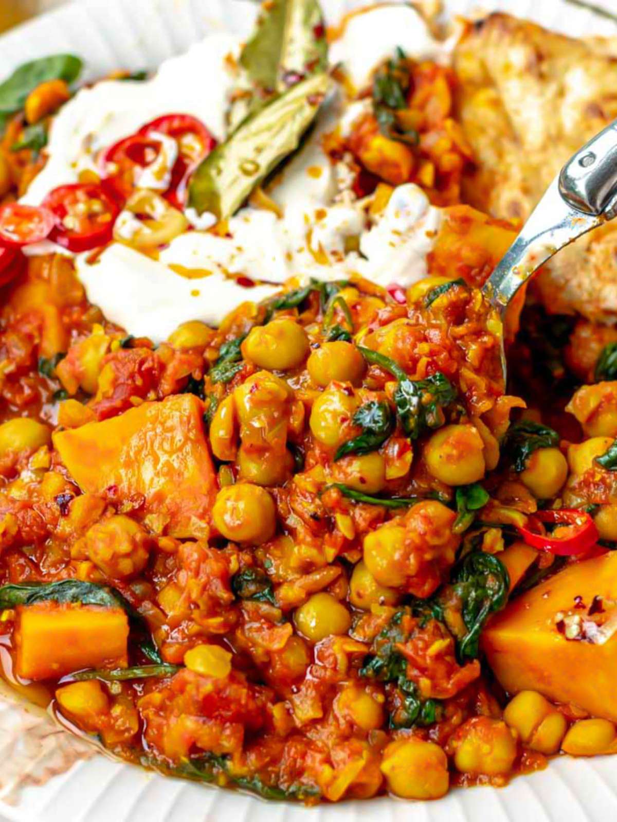 Creamy turmeric chickpea stew with sweet potatoes and spinach on a white plate.