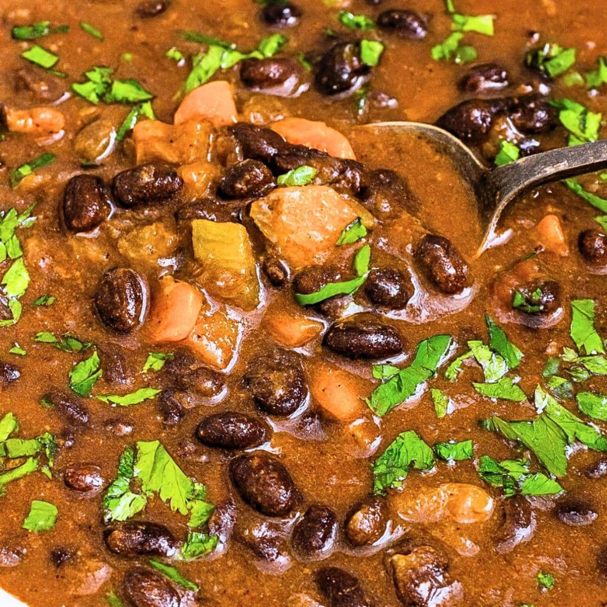 Easy black bean soup in a rustic bowl with fresh herbs and a spoon.