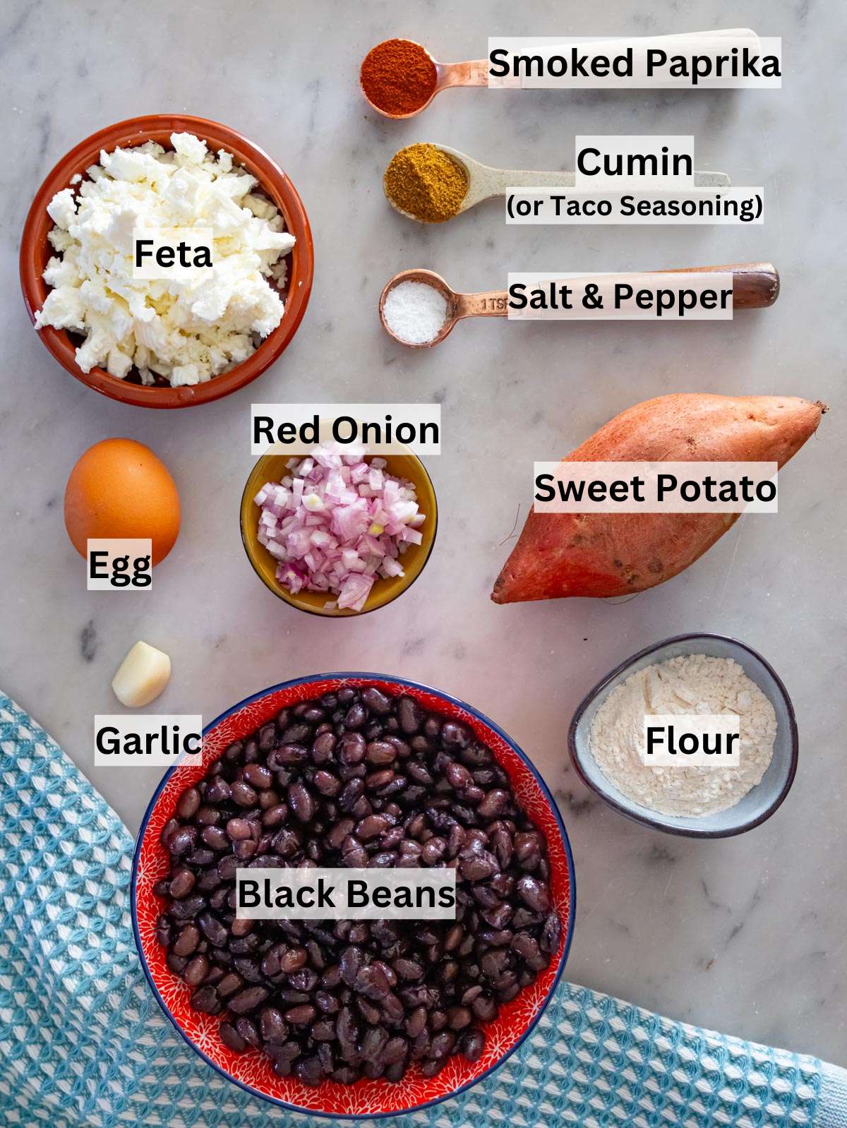 Fresh ingredients for black bean patties including beans sweet potato feta and spices on countertop.