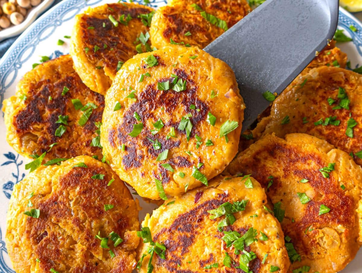 Healthy chickpea sweet potato patties on a marble table with dip and lemon wedges.