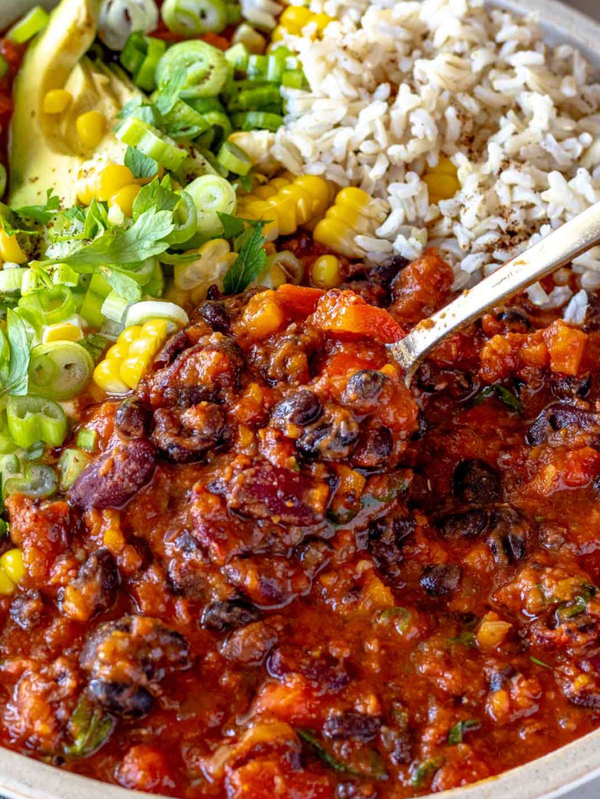 Hearty chili with beans in a bowl topped with avocado and cilantro.