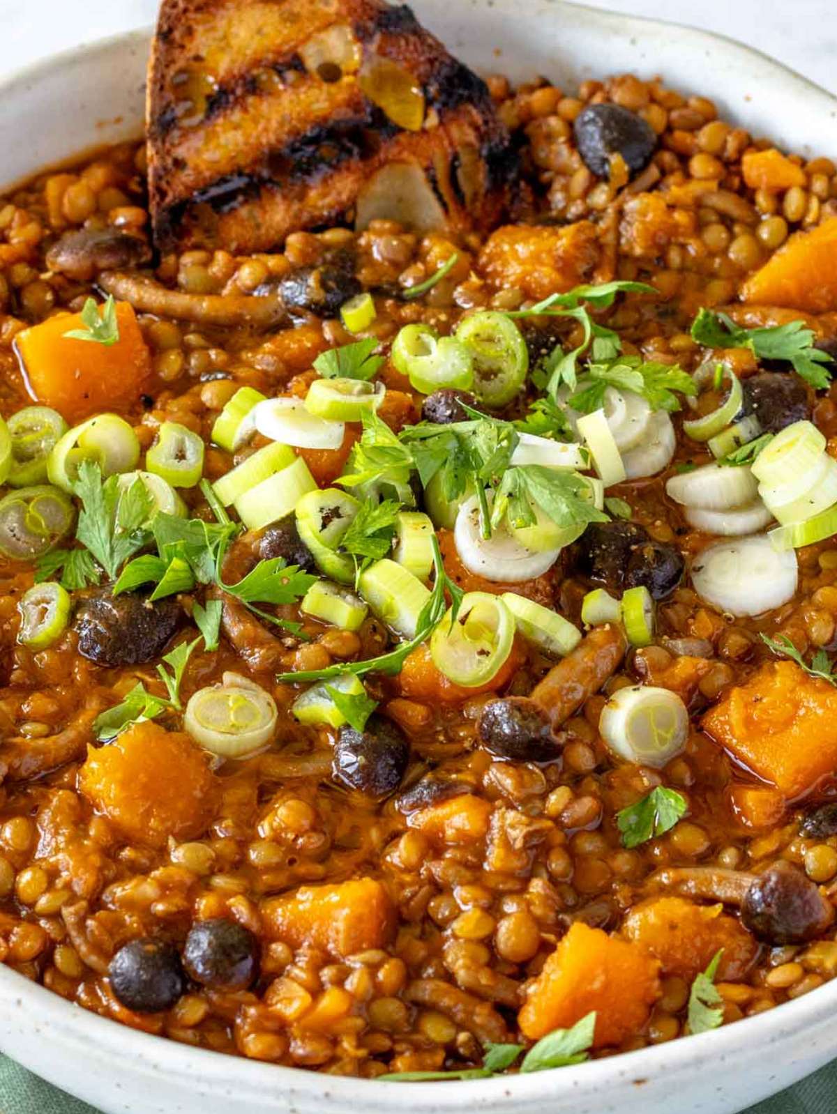 Hearty lentil pumpkin stew in a bowl topped with olive oil and fresh herbs.
