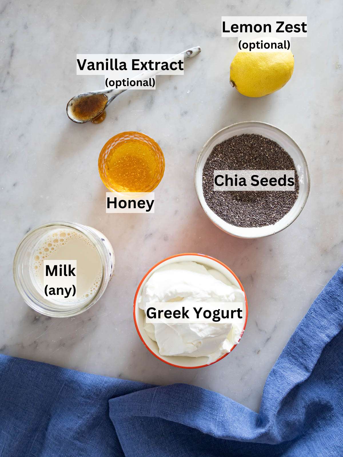 Ingredients for Greek yogurt chia pudding arranged neatly on a white table with chia seeds and yogurt.