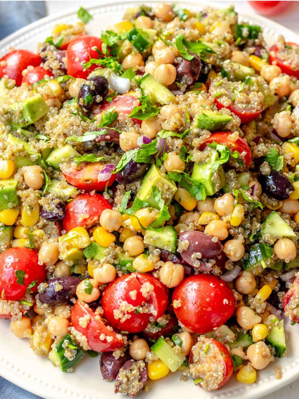 Mediterranean quinoa salad with avocado tomato cucumber and olives on a platter.