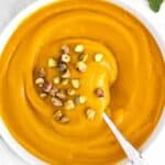 Rustic bowl of Mediterranean pumpkin soup with pistachios and fresh rosemary sprigs.