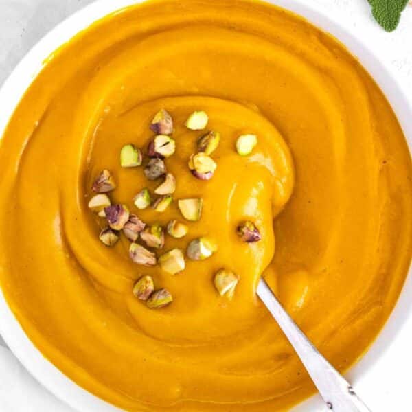 Rustic bowl of Mediterranean pumpkin soup with pistachios and fresh rosemary sprigs.