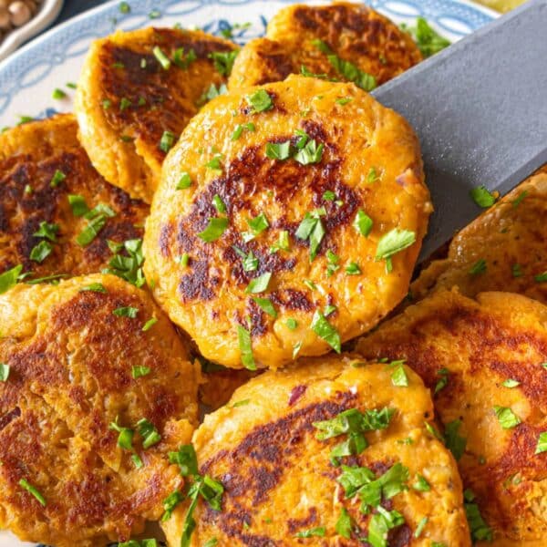 Stack of crispy chickpea sweet potato patties on a white and blue plate with herbs.