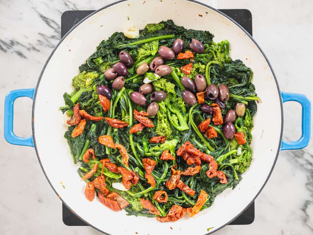Step 2 Broccoli rabe cooking in a pan with sun-dried tomatoes and olives.