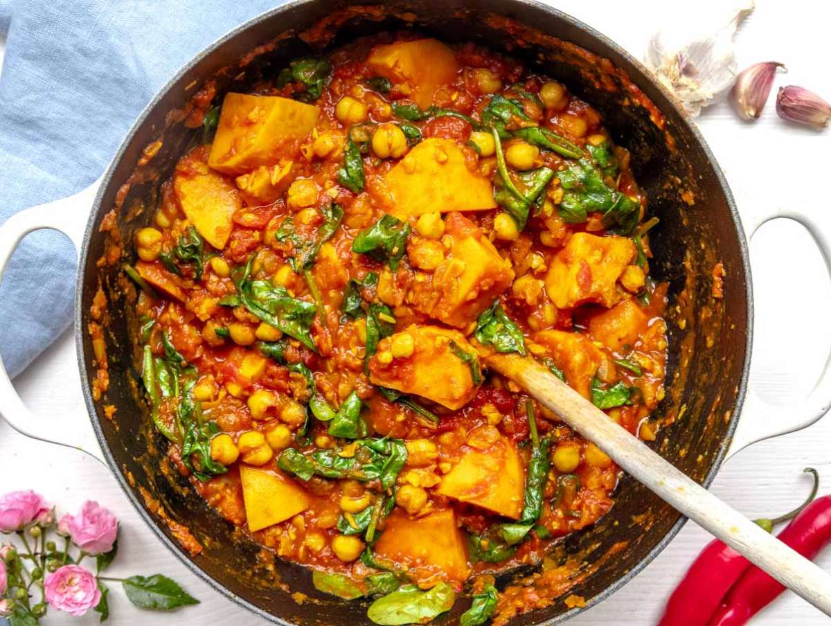 Step 3 – Stirring fresh spinach into turmeric chickpea stew until wilted and vibrant green.