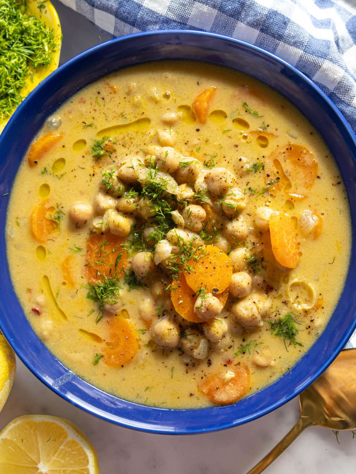Top-down view of Greek chickpea soup in blue bowl with lemon and parsley garnish.