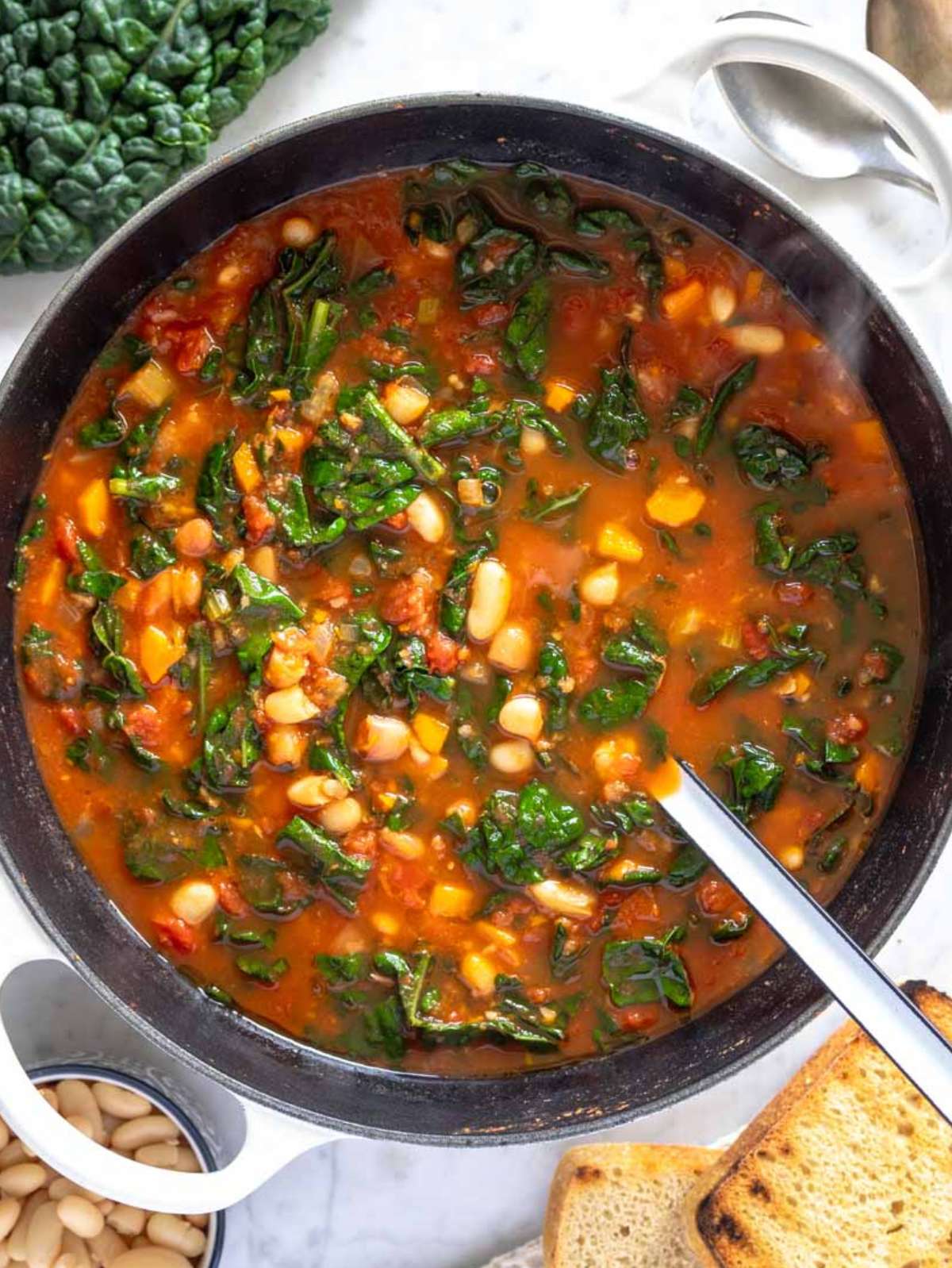 Top-down view of Mediterranean kale soup with bread and olive oil drizzle.