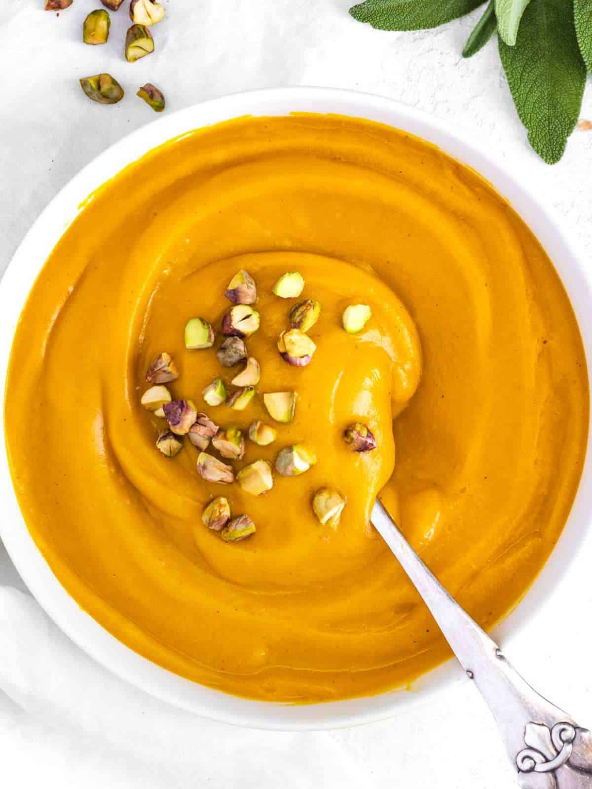 Top down view of Mediterranean pumpkin soup served with pistachios and herbs.