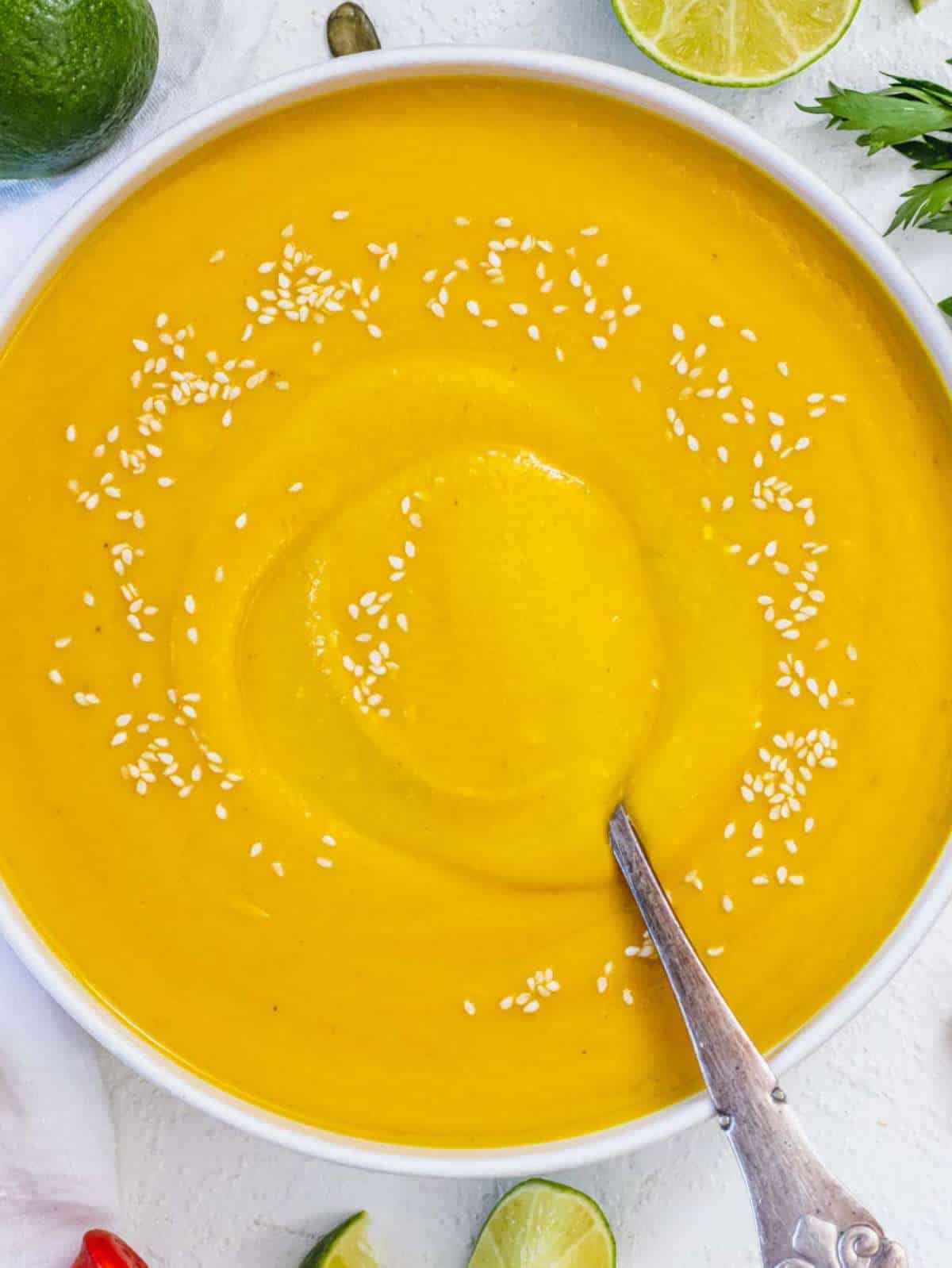 Top down view of coconut pumpkin soup garnished with lime wedges and fresh cilantro.