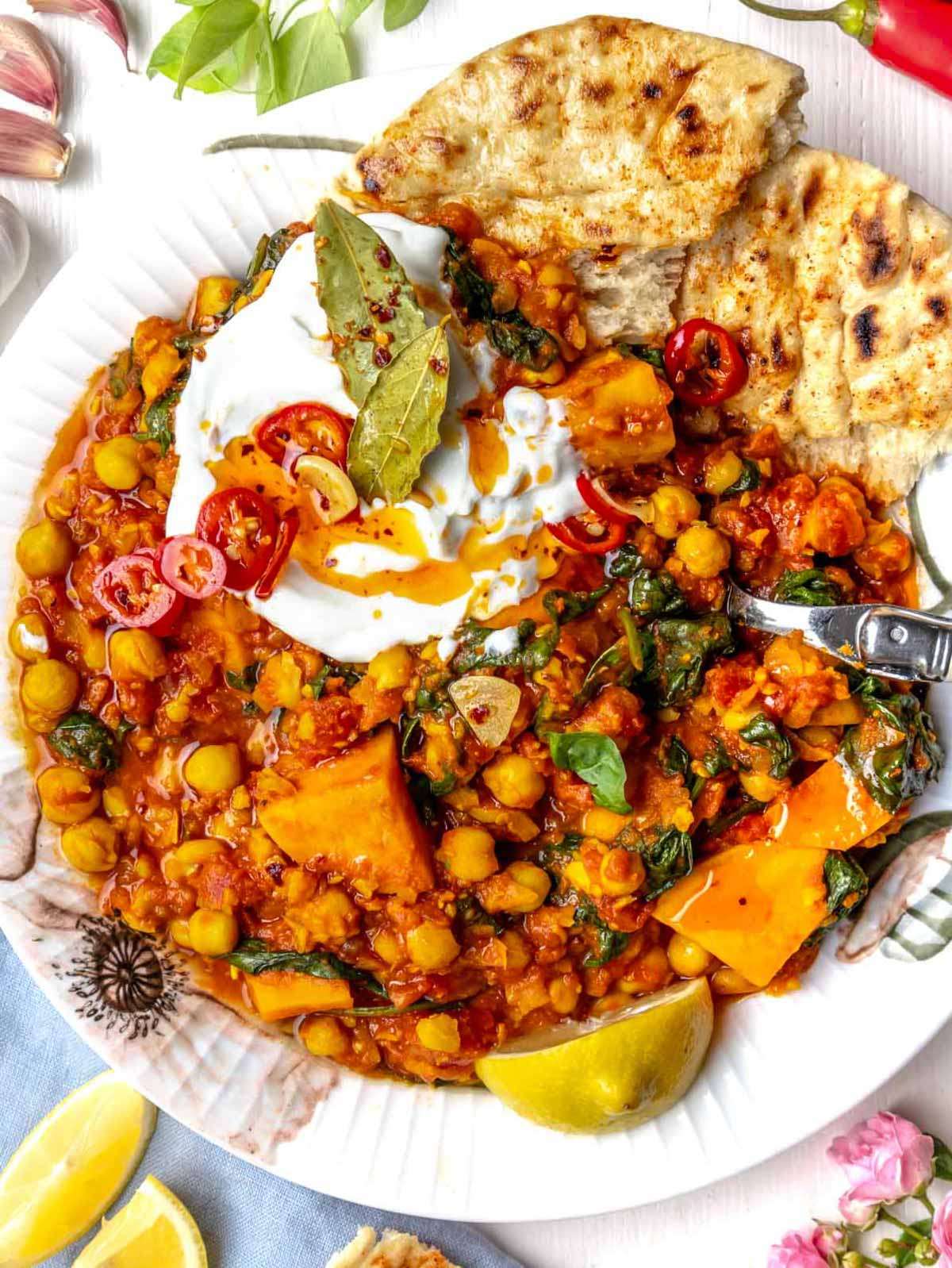 Top view of turmeric chickpea stew served with lemon wedges and fresh herbs.