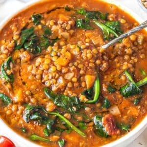 Warm bowl of spinach lentil soup with olive oil drizzle and lemon wedge.