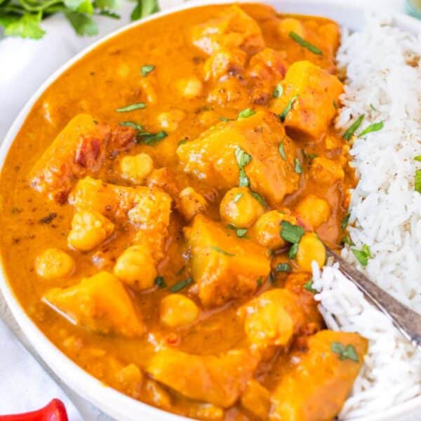 White bowl of butternut squash chickpea curry with basmati rice and fresh cilantro on table.
