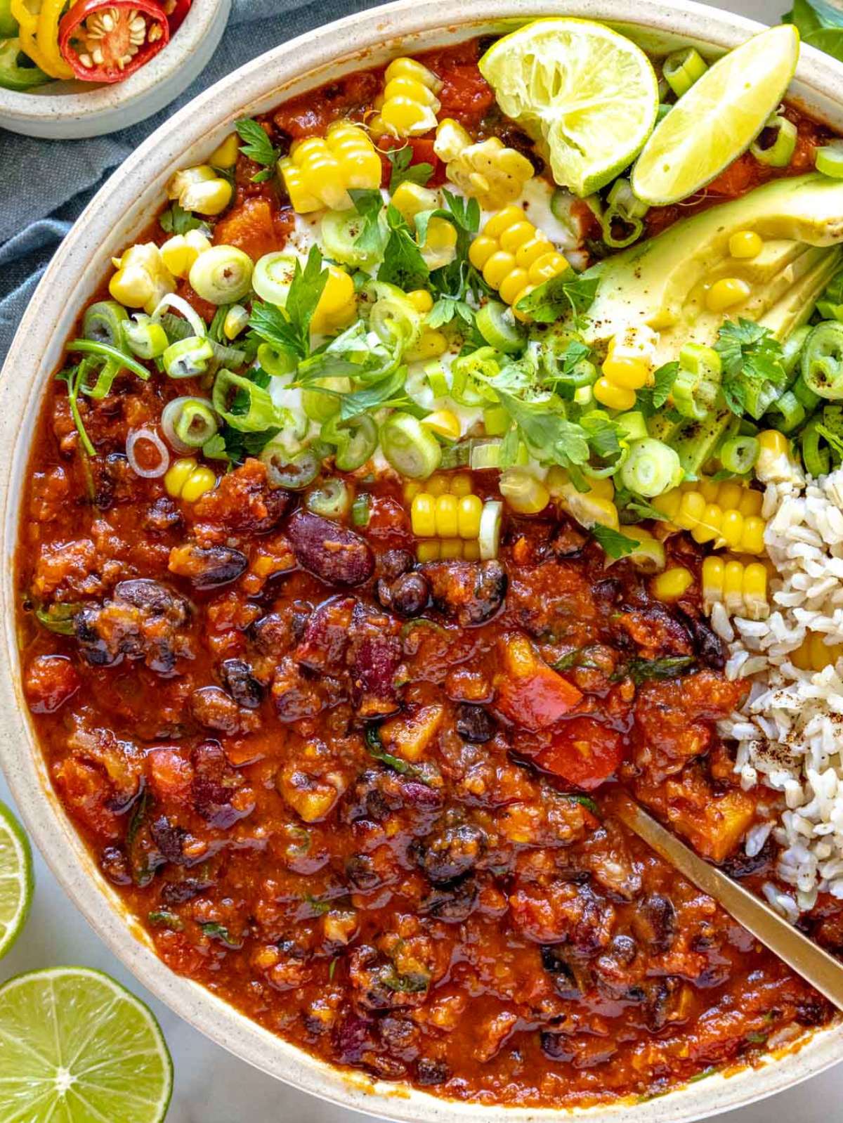 antro Top down view of chili with beans served with corn avocado and lime.