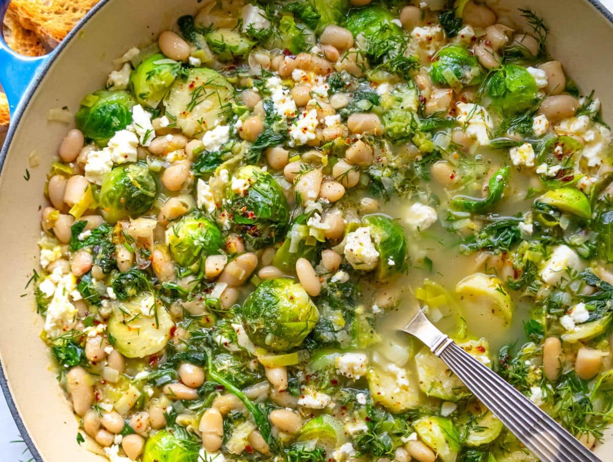 Close up of bright Mediterranean greens and beans topped with feta and fresh herbs.