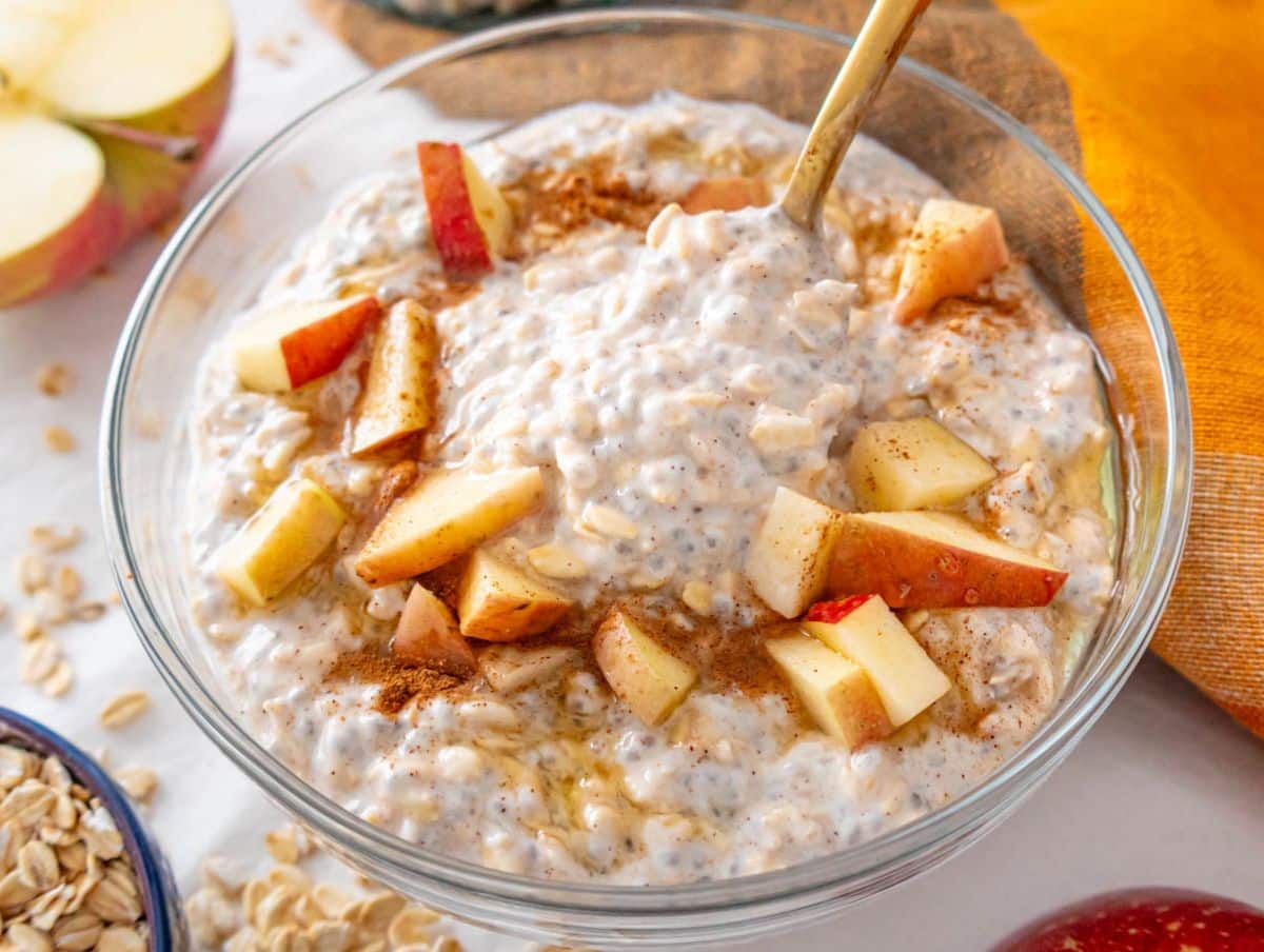 Close-up of creamy apple cinnamon overnight oats in a glass bowl with diced apples and cinnamon sprinkle.