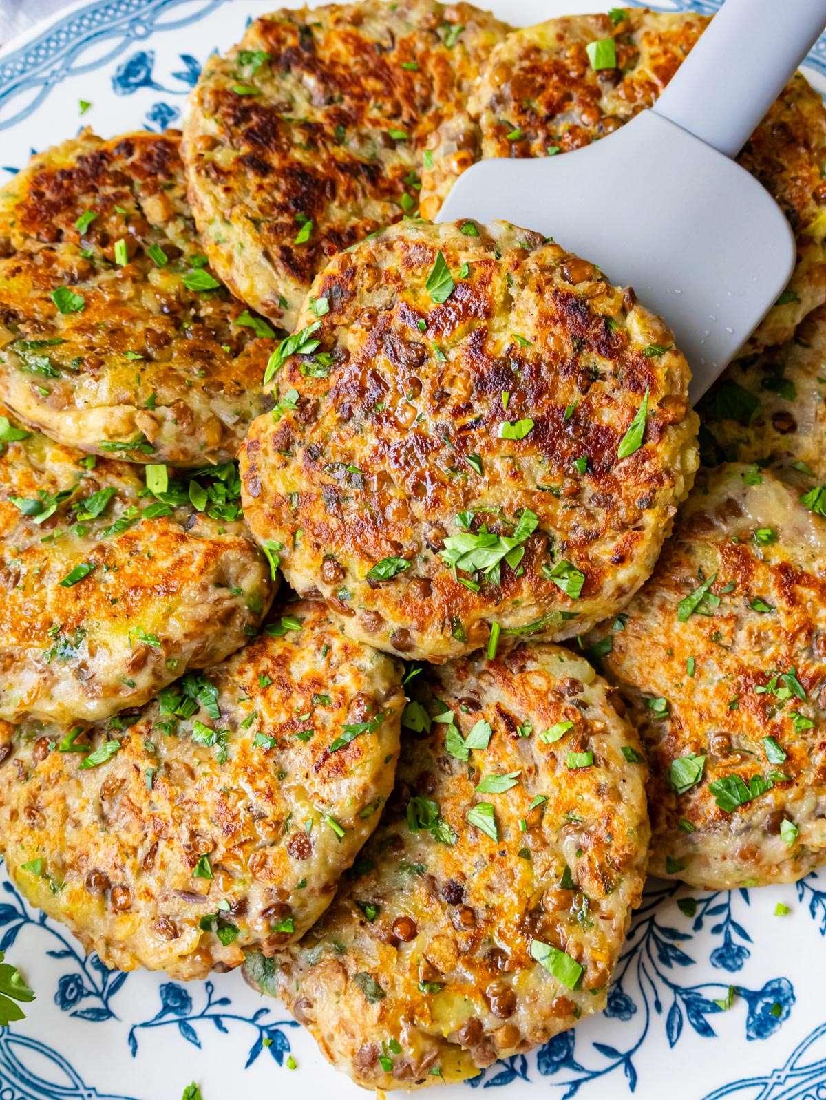 Close up picture of crispy lentil potato patties stacked on a plate with fresh herbs.