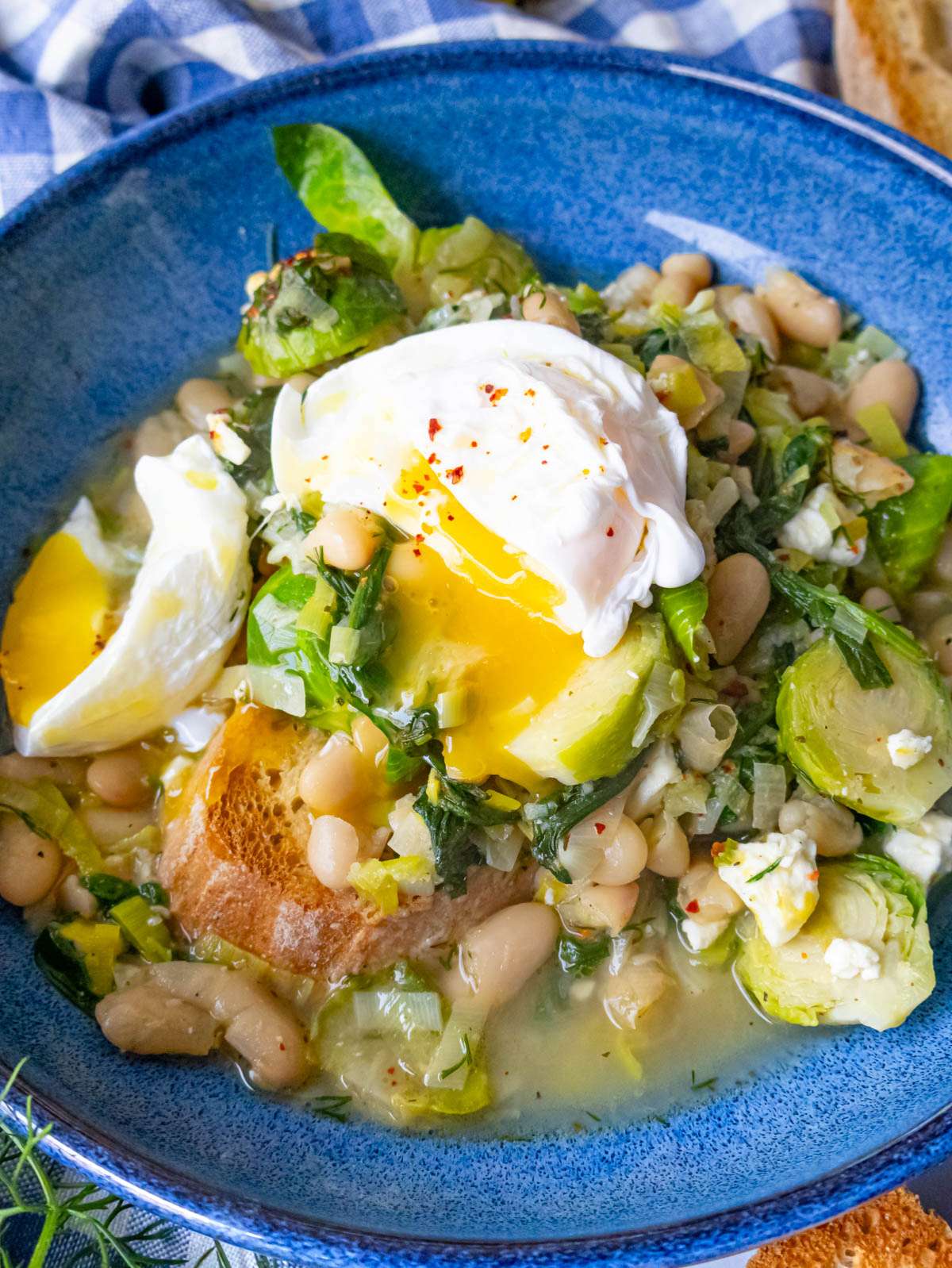 Creamy Mediterranean greens and beans close up in a bowl served with a poached egg.
