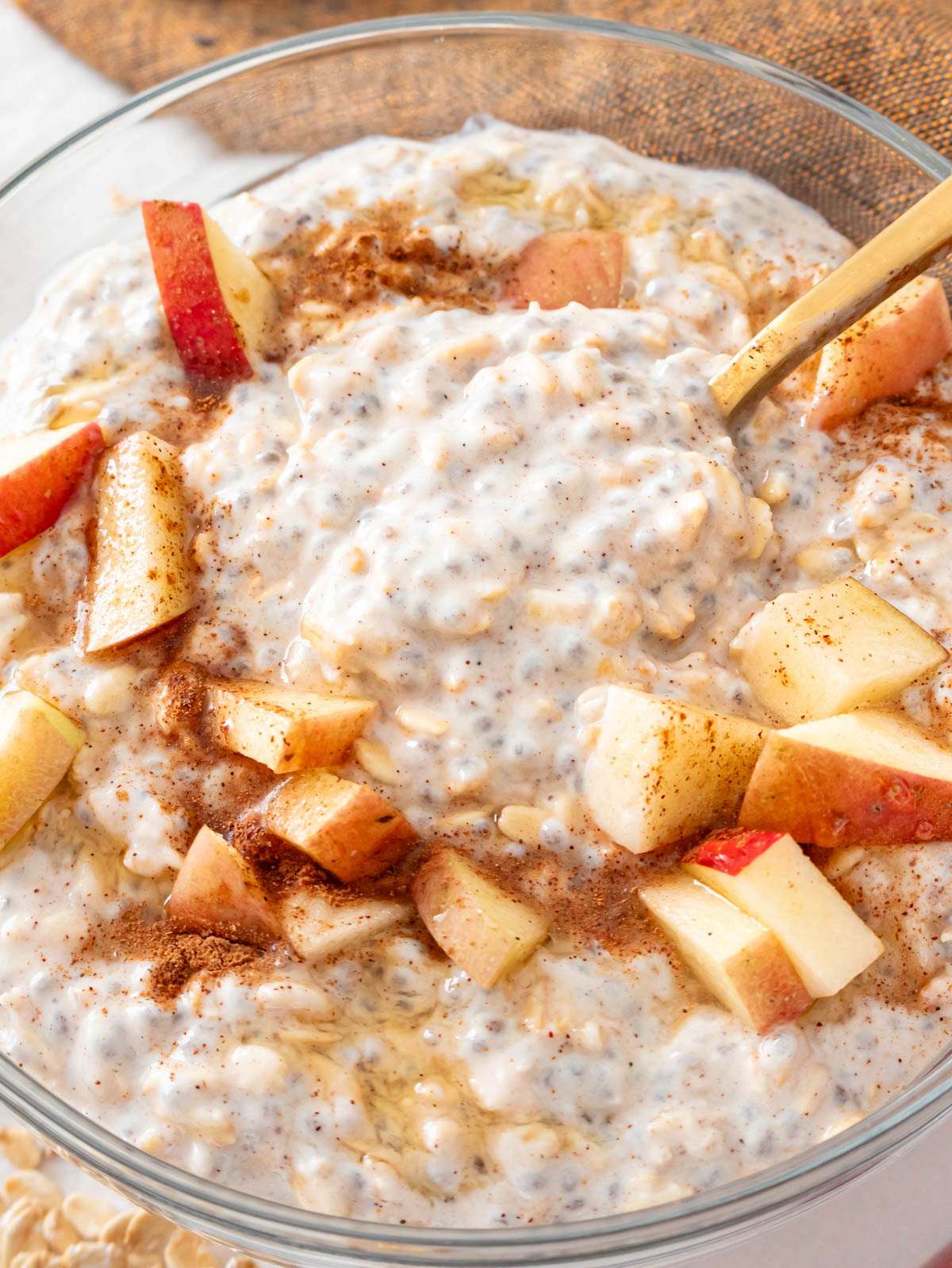 Creamy apple cinnamon overnight oats in a glass bowl topped with apples and cinnamon.
