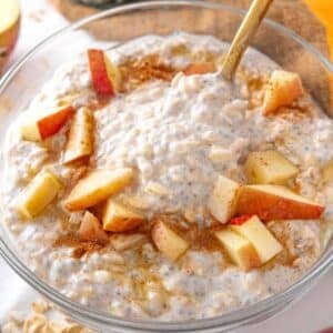 Feature image of apple cinnamon overnight oats in a glass bowl topped with fresh apples and cinnamon.