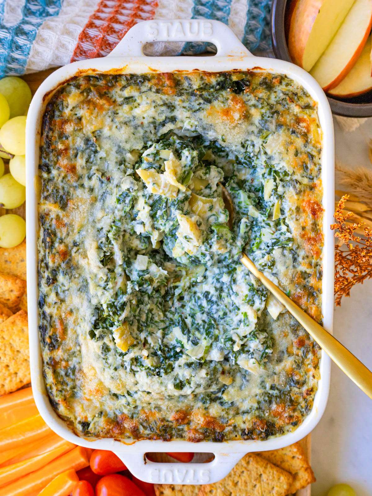 Finished dip top down with golden parmesan crust spoon in and crackers and veggies on the side.